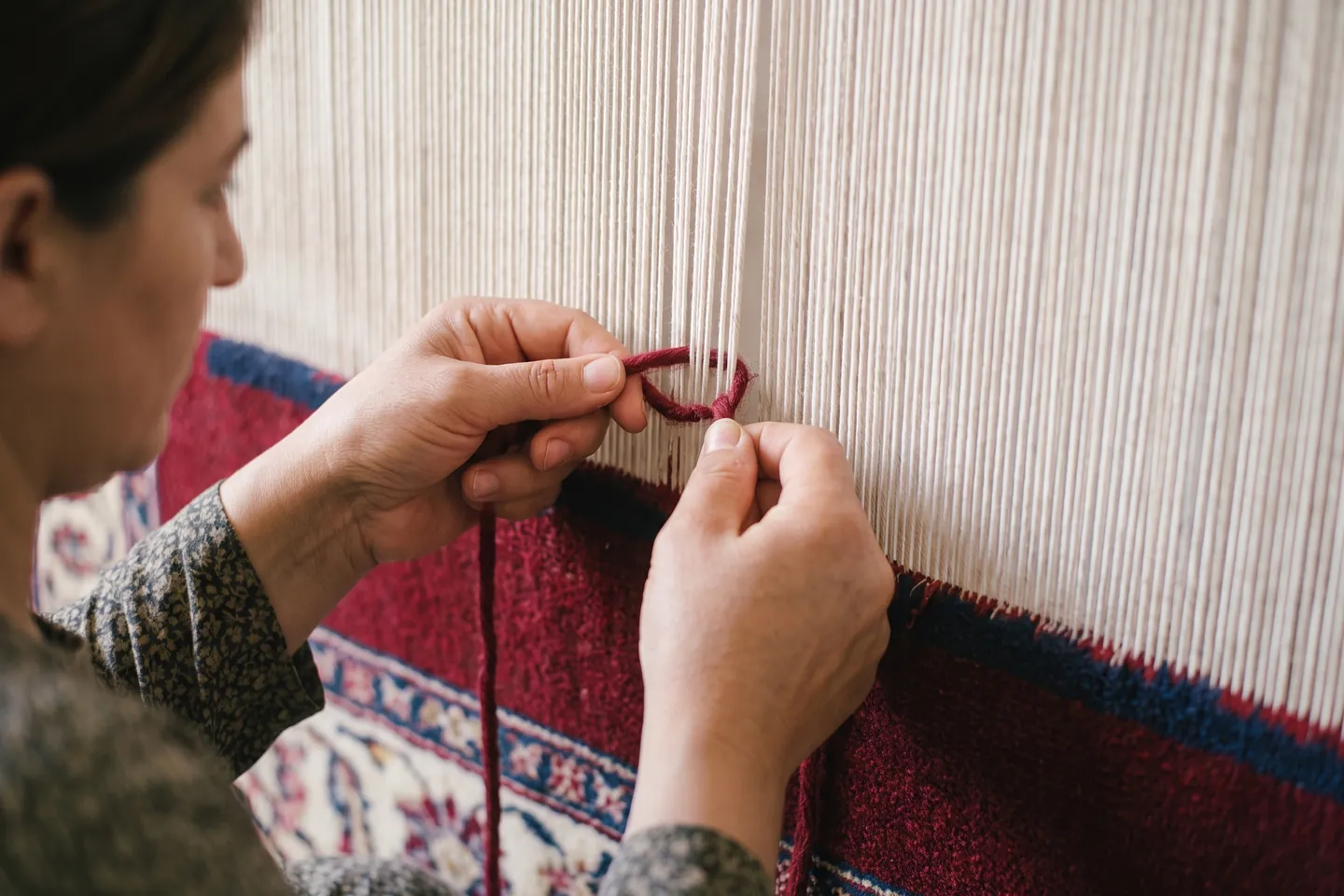 A weaver tying knots row by row on an upright loom